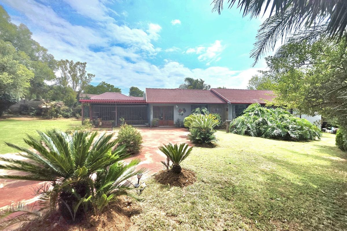 A rear view of the residential property featuring a tiled roof, a covered patio area, and a spacious landscaped garden with paved courtyard.