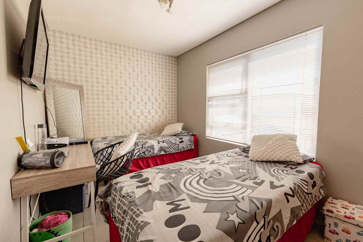 A functional bedroom featuring patterned wallpaper, neutral wall paint, and a large window fitted with venetian blinds.