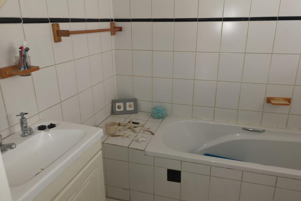A functional bathroom featuring a built-in bathtub, vanity basin, and white wall tiling with a decorative black accent border.