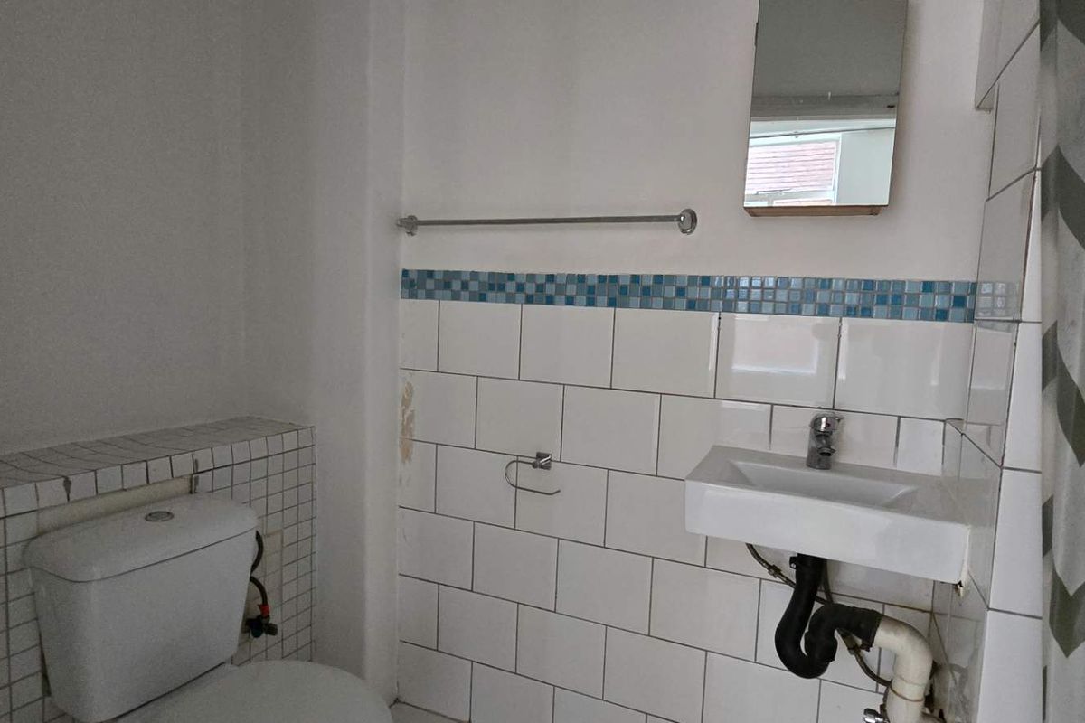 A compact bathroom featuring a wall-mounted basin, toilet, and tiled splashback. The space requires minor repairs to wall finishes and plumbing fixtures.