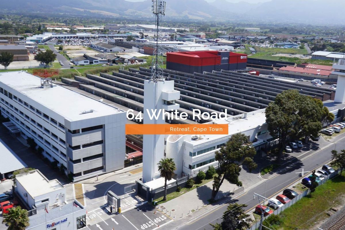 Aerial view of a large industrial facility featuring a multi-story office building, warehouse complex, telecommunications tower, and secure gated parking area.