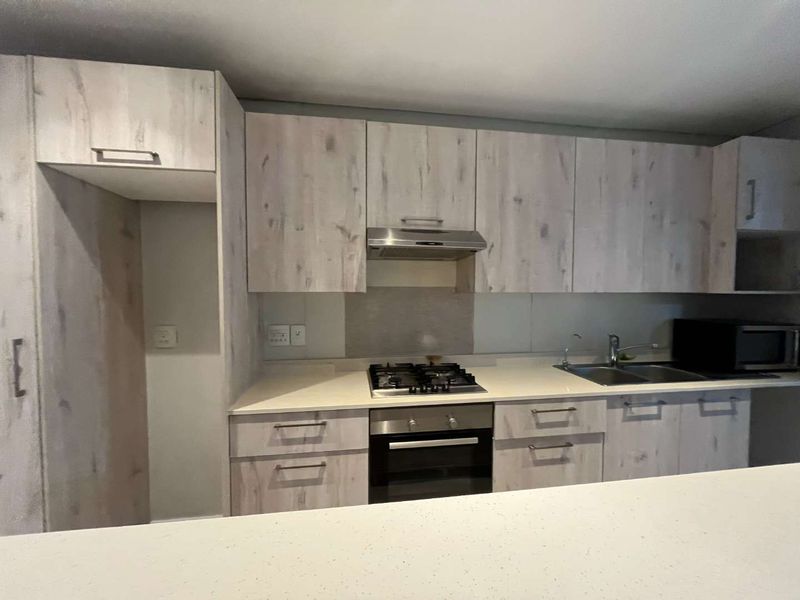 Modern kitchen featuring light wood-grain cabinetry, stone countertops, a gas hob, built-in oven, and a convenient breakfast bar for casual dining.