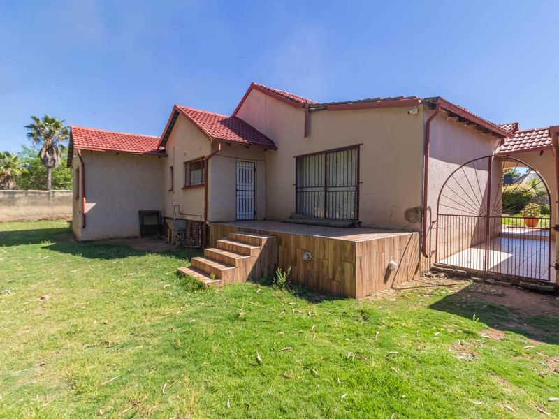 Rear view of the house featuring a tiled patio area, security gates, and terracotta roof tiles set within a spacious garden.