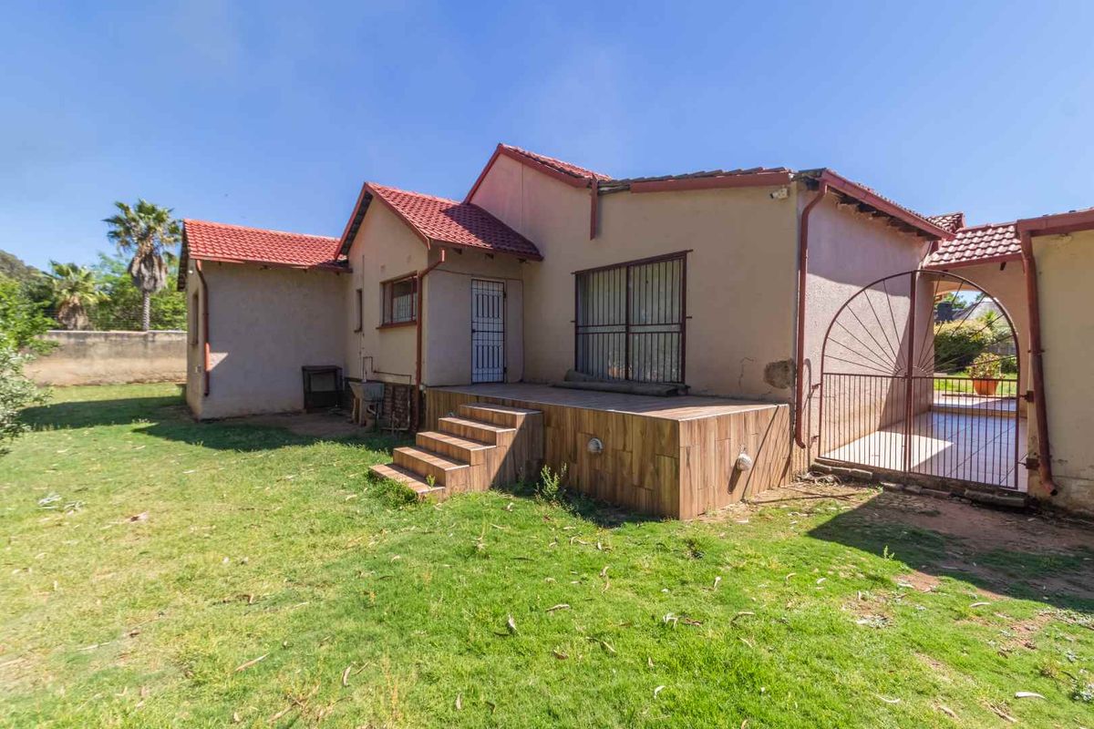 Rear view of the house featuring a tiled patio area, security gates, and terracotta roof tiles set within a spacious garden.