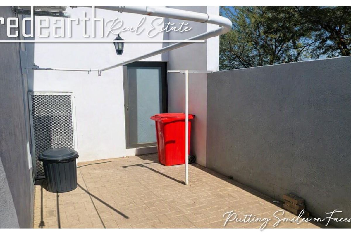 A paved rear courtyard area featuring a perimeter wall, security gate, and wall-mounted clothesline.