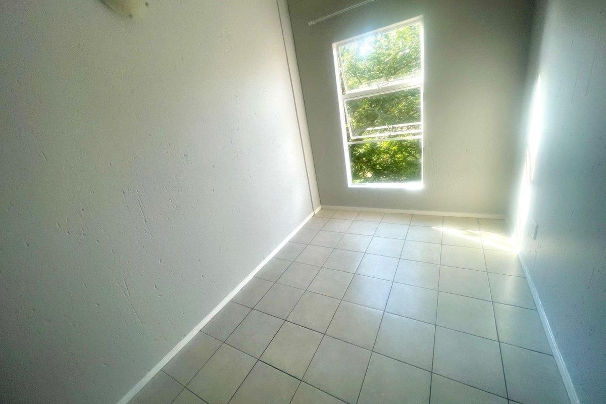 An empty bedroom featuring tiled flooring and a large window, providing a blank canvas for potential interior design and renovation.