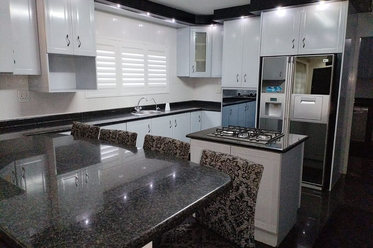 Modern kitchen featuring high-gloss white cabinetry, dark granite countertops, a central island with a gas hob, and integrated lighting.