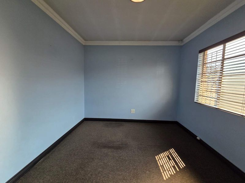 A vacant office space featuring blue walls, carpet flooring, and window blinds, providing a clean and functional environment for a workspace.