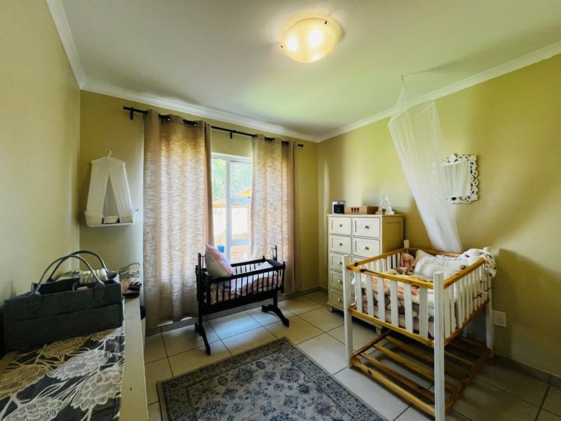 A functional bedroom featuring tiled flooring and a central ceiling light fixture, currently utilized as a nursery with natural light from the window.