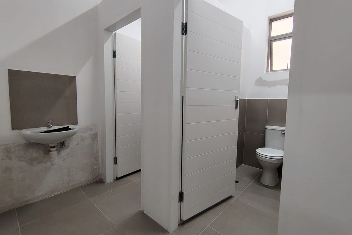 A functional office restroom featuring tiled flooring, a wall-mounted basin, and a private toilet cubicle with modern white doors.