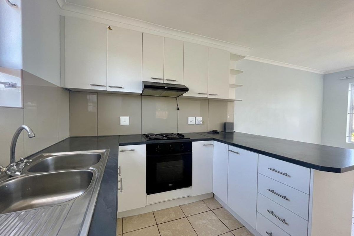 A clean, functional kitchen featuring white cabinetry, dark countertops, a built-in oven, gas hob, extractor fan, and a double stainless steel sink.