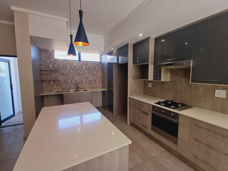Modern kitchen featuring a central island, stone countertops, built-in oven, gas hob, extractor fan, and ample cabinetry with a stylish tiled backsplash.