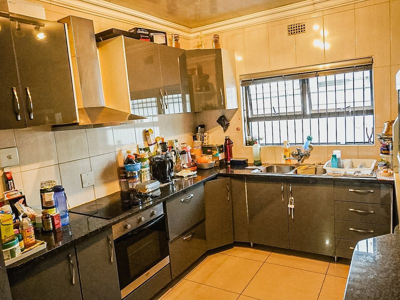 Functional kitchen featuring dark grey cabinetry, granite countertops, built-in oven, electric hob, and tiled splashbacks with security bars on the window.