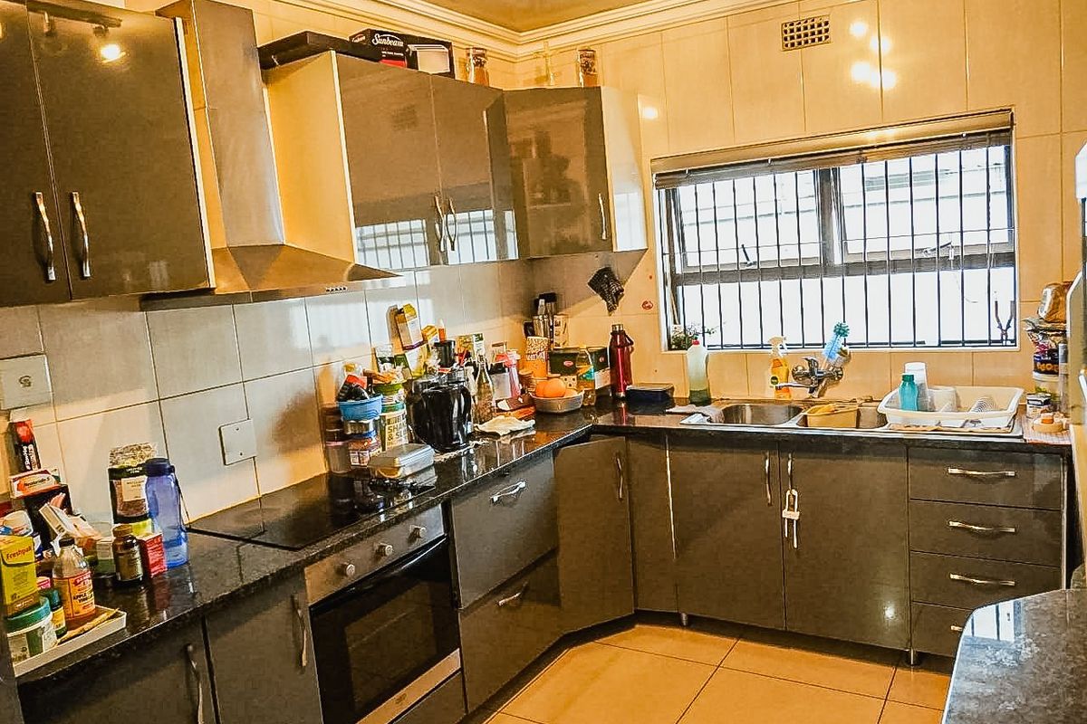 Functional kitchen featuring dark grey cabinetry, granite countertops, built-in oven, electric hob, and tiled splashbacks with security bars on the window.