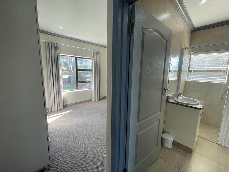 A bright, carpeted bedroom featuring an en-suite bathroom with a modern vanity and shower enclosure, offering a clean and functional living space.