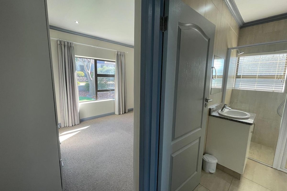 A bright, carpeted bedroom featuring an en-suite bathroom with a modern vanity and shower enclosure, offering a clean and functional living space.
