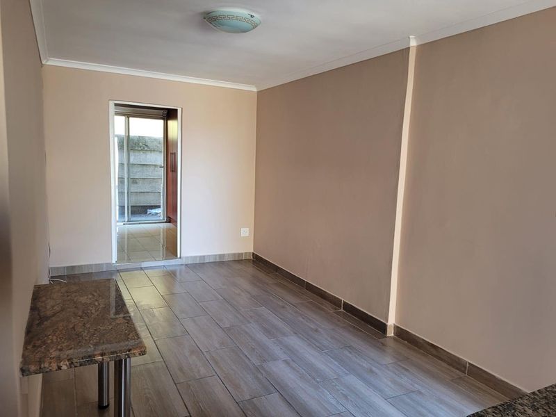 An empty living area featuring modern wood-look floor tiles, neutral wall tones, and a granite breakfast bar, leading to an outdoor space.