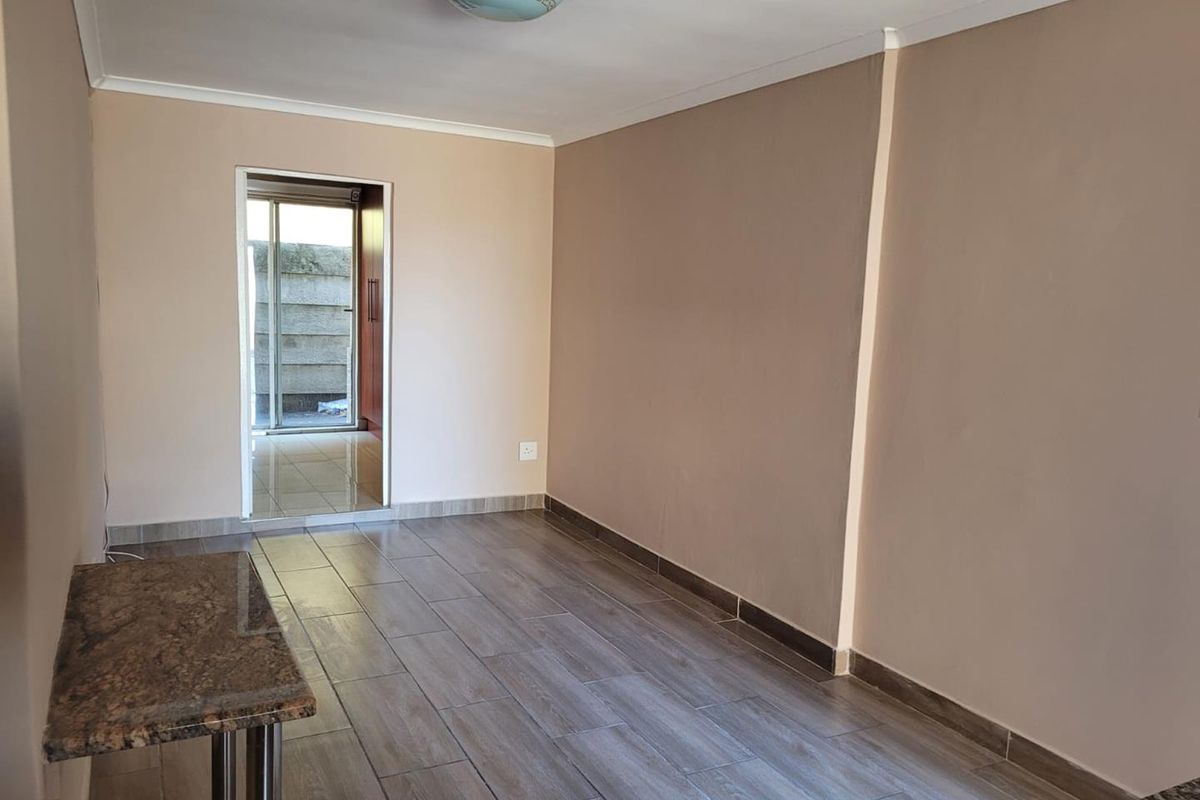 An empty living area featuring modern wood-look floor tiles, neutral wall tones, and a granite breakfast bar, leading to an outdoor space.