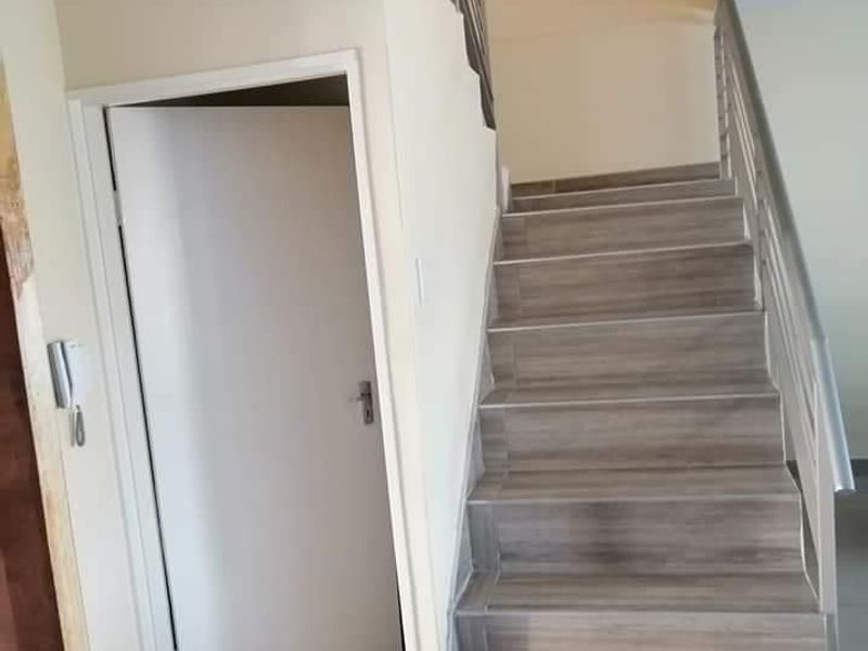 A bright hallway featuring a staircase with wood-look tiled steps and a metal handrail, leading to an upper level.