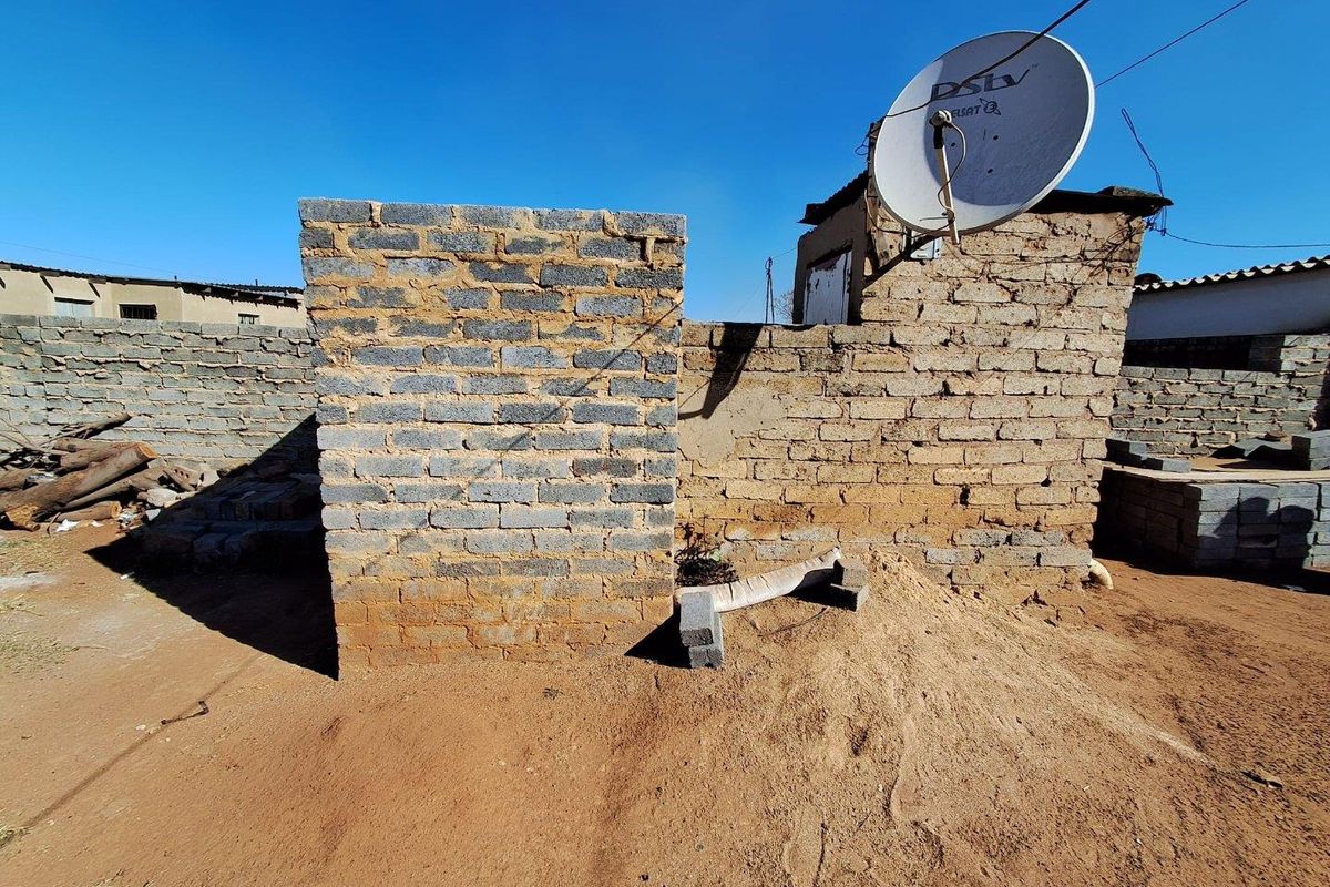 View of a residential backyard featuring unfinished brick wall structures and a mounted satellite dish on a sandy plot.
