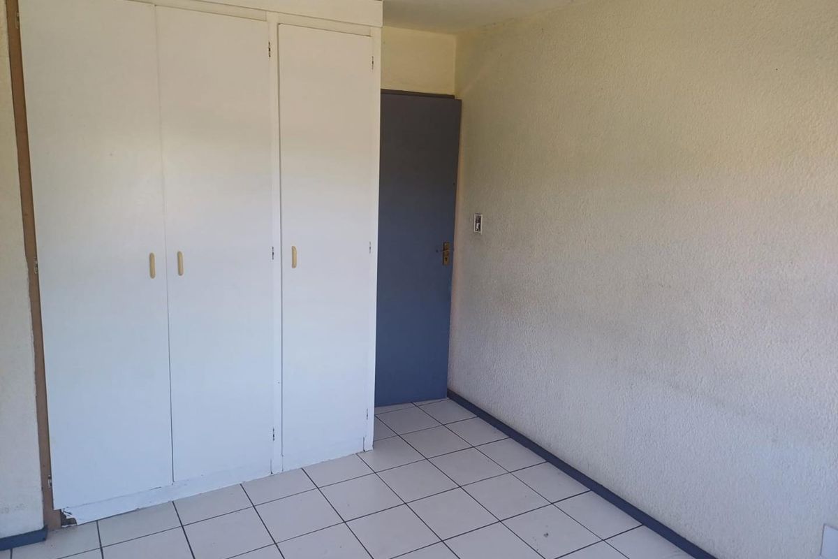 An empty bedroom featuring white built-in cupboards and tiled flooring, providing a blank canvas for personalization.
