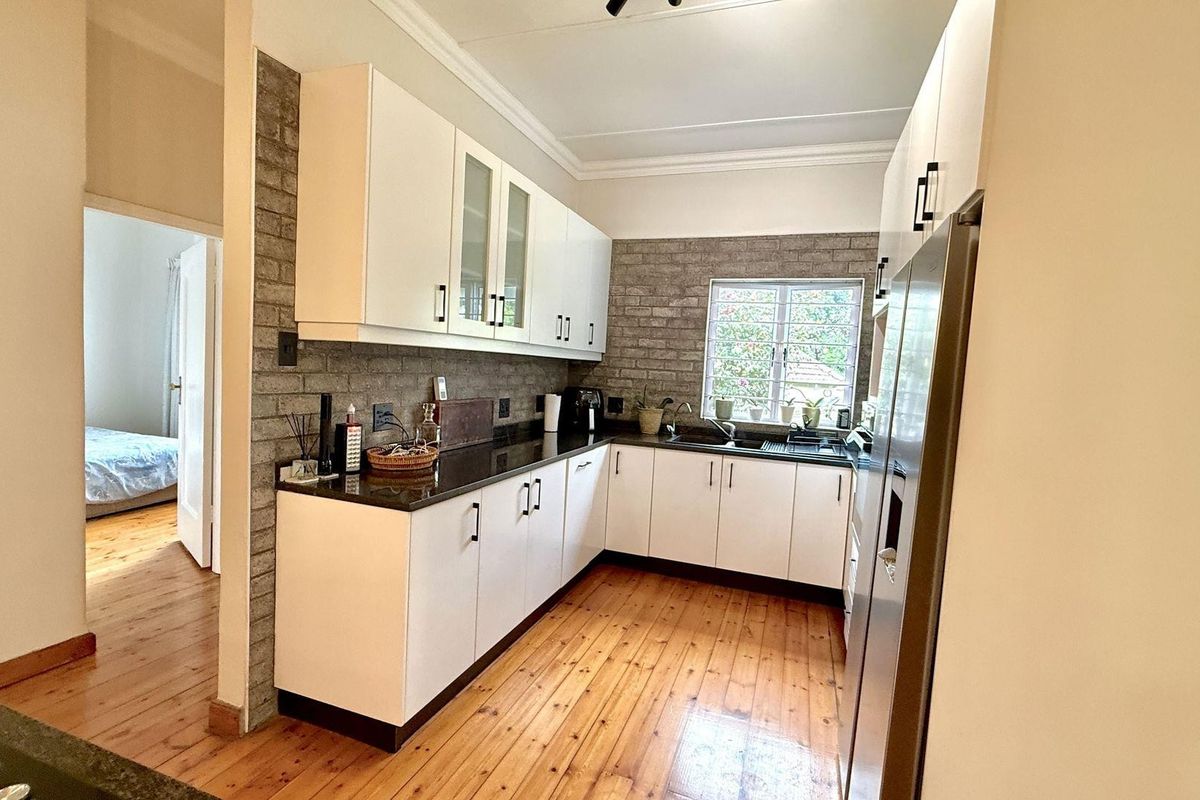 A well-lit kitchen featuring white cabinetry, dark stone countertops, and a distinctive brick-style feature wall, complemented by warm timber flooring.