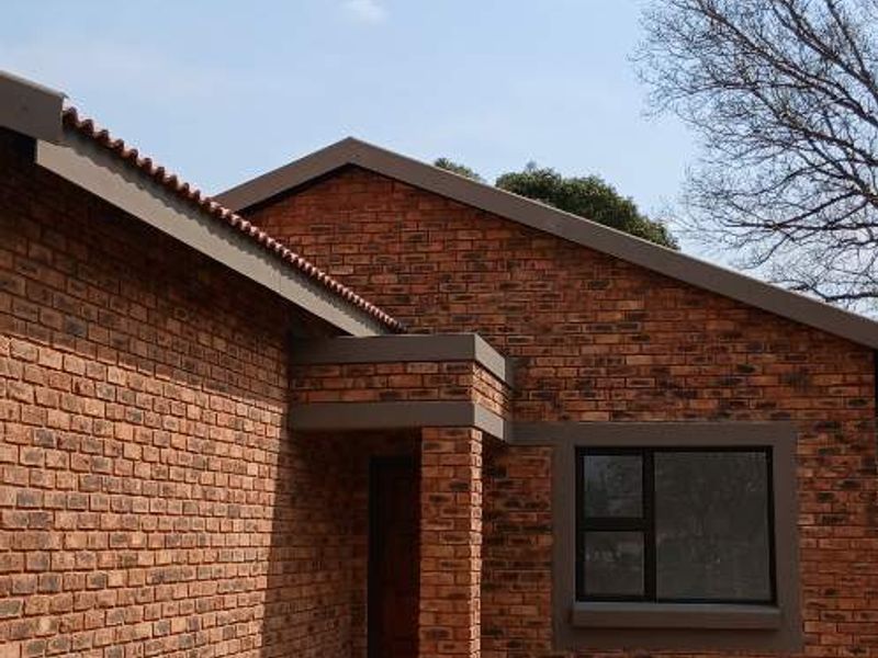 A well-maintained face brick exterior facade featuring a paved walkway and modern aluminium window frames.