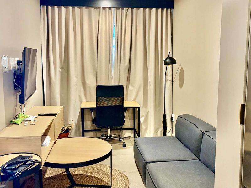 A compact living area featuring neutral wall tones, tiled flooring, and floor-to-ceiling curtains, providing a functional and well-lit space.