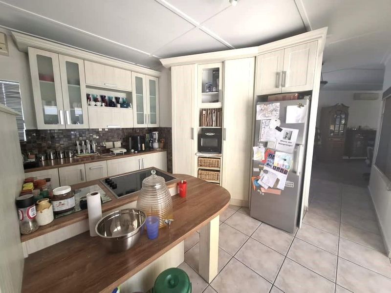 A functional kitchen featuring light-toned built-in cabinetry, a tiled backsplash, a central island with an integrated hob, and tiled flooring throughout.