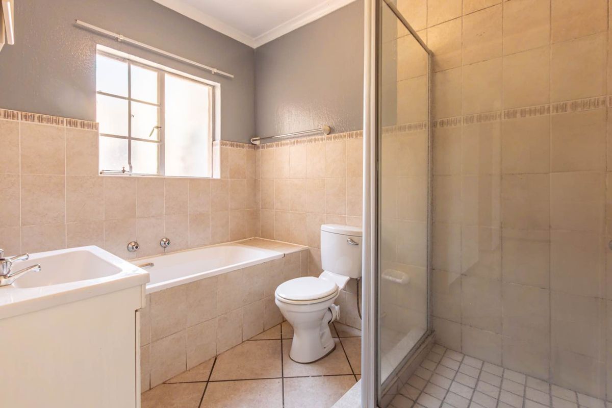 A functional bathroom featuring a built-in bathtub, separate shower enclosure, toilet, and vanity basin with neutral wall and floor tiling.