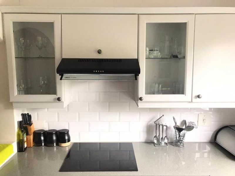A well-maintained kitchen area featuring a modern induction cooktop, subway tile backsplash, and elegant glass-front cabinetry with integrated extractor fan.