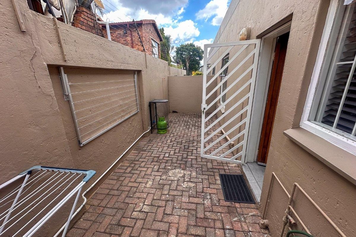 A private rear courtyard featuring brick paving, a wall-mounted drying rack, and a security gate providing access to the apartment.