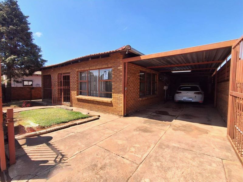 Front view of a face brick house featuring a paved driveway, attached carport, and secure metal fencing.
