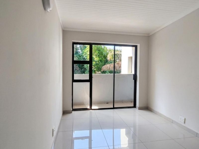 A bright, empty bedroom featuring polished white floor tiles, a tongue and groove ceiling, and a sliding glass door leading to an outdoor area.
