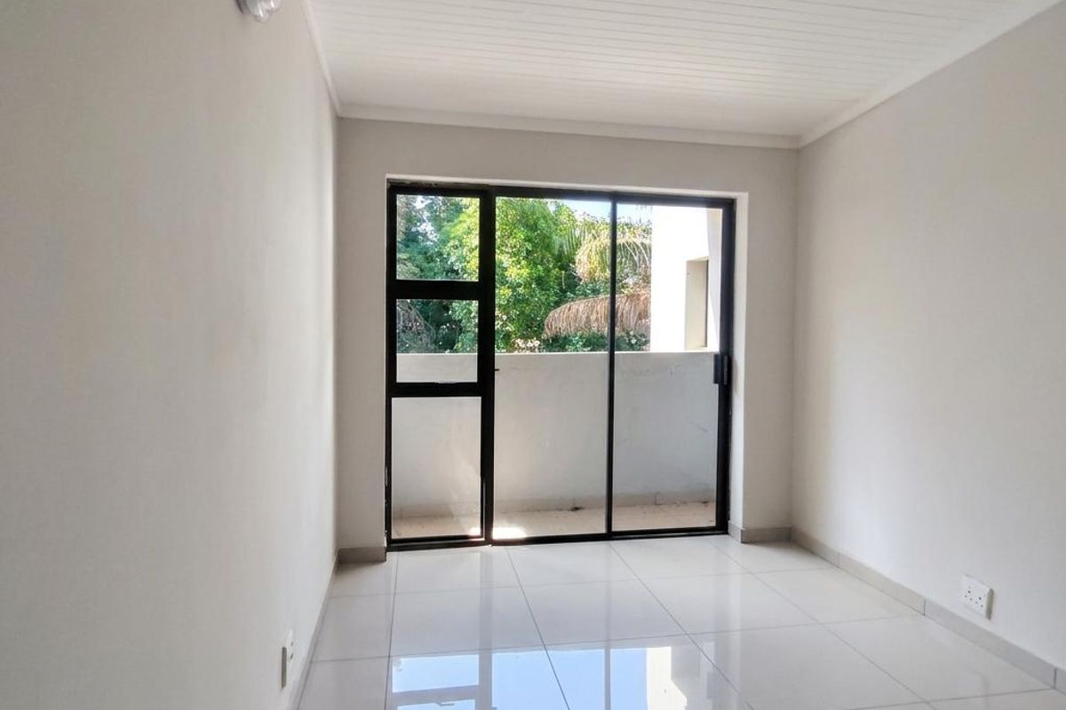 A bright, empty bedroom featuring polished white floor tiles, a tongue and groove ceiling, and a sliding glass door leading to an outdoor area.
