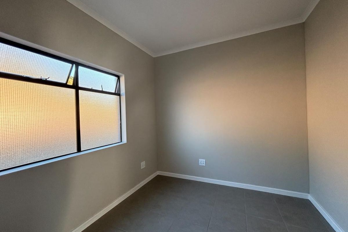 A clean, empty bedroom featuring neutral wall paint, tiled flooring, and a window with security mesh.