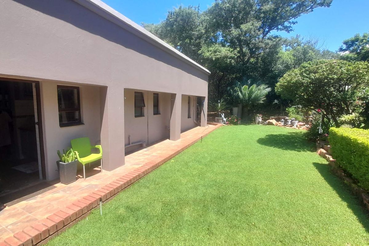 A view of the rear exterior featuring a covered patio with tiled flooring, brick edging, and a well-maintained lawn garden.