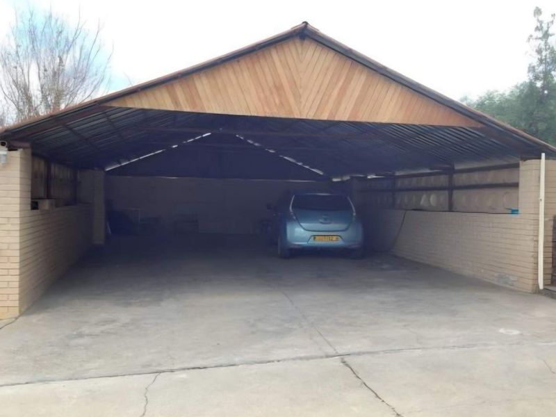 A spacious open-sided garage featuring a concrete floor, brick walls, and a timber-clad gable roof structure.