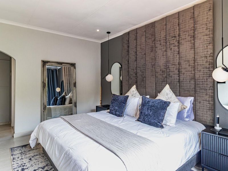 A well-appointed bedroom featuring a large upholstered feature wall, built-in cupboards, and modern pendant lighting.