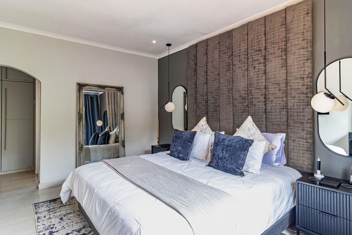 A well-appointed bedroom featuring a large upholstered feature wall, built-in cupboards, and modern pendant lighting.