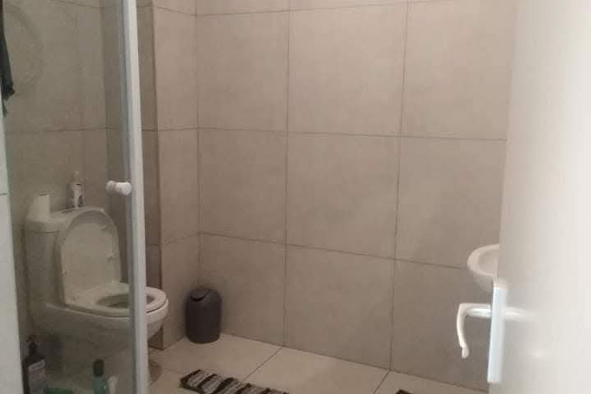 A functional bathroom featuring a glass-enclosed shower, toilet, and washbasin with neutral wall and floor tiling.