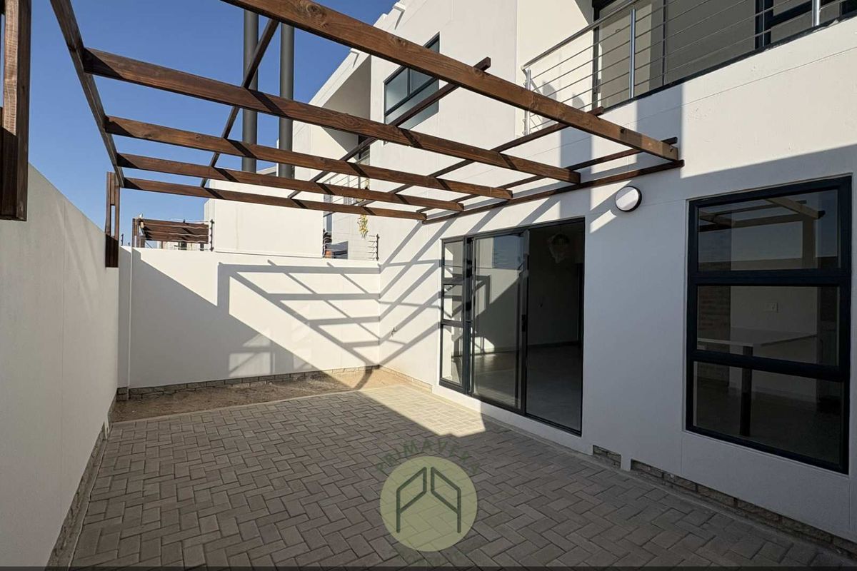 A private rear patio area featuring paved flooring, a wooden pergola structure, and direct access to the interior through sliding glass doors.