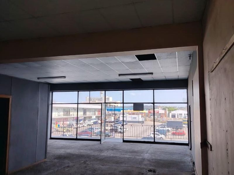 An empty, open-plan commercial space featuring large glass windows, a suspended ceiling, and worn concrete flooring, suitable for retail or office use.