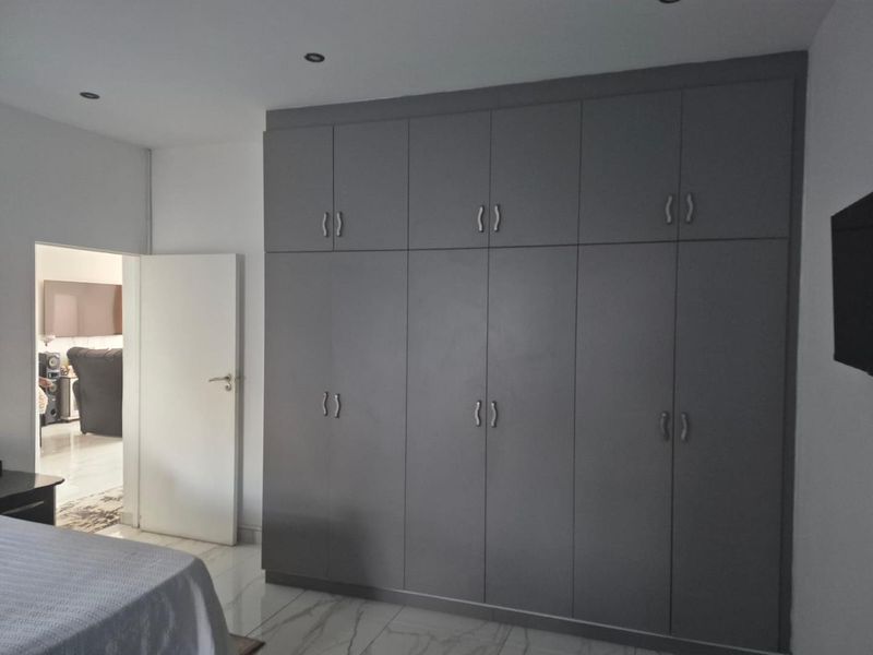 A bedroom featuring modern grey floor-to-ceiling built-in cupboards, recessed downlighting, and polished tiled flooring.