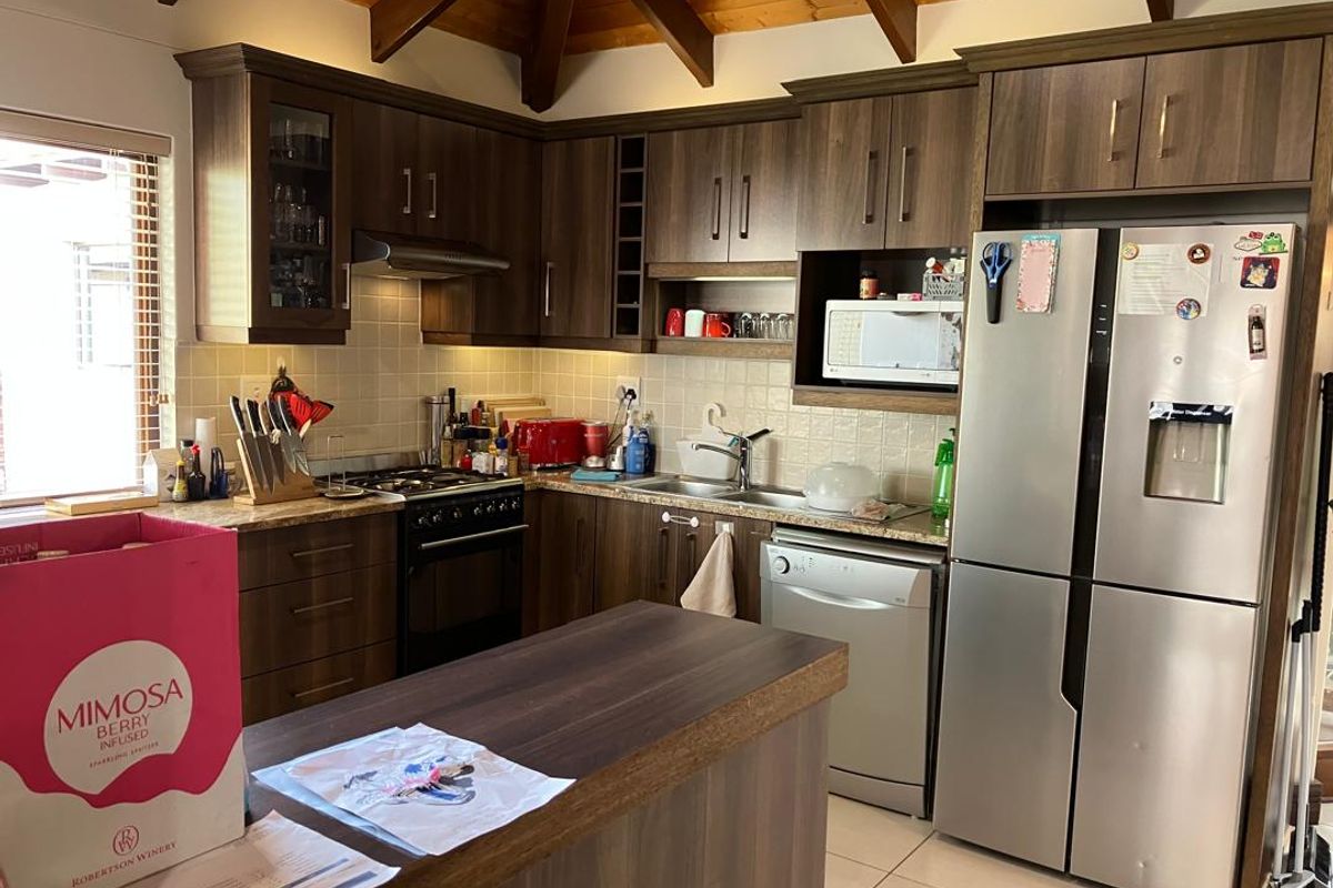 A functional kitchen featuring dark wood cabinetry, tiled backsplash, stainless steel appliances, and a central island under a vaulted timber-beamed ceiling.
