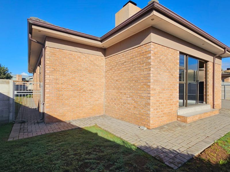 Rear view of the house featuring a face brick facade, paved patio area, and sliding glass doors leading to the interior.