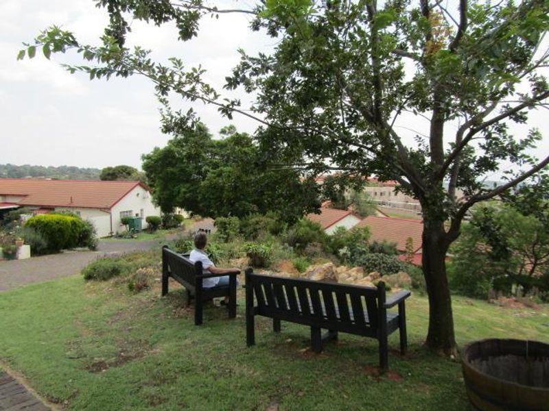 A peaceful landscaped garden area within the retirement village, featuring mature trees, established shrubs, and views over the surrounding residential complex.