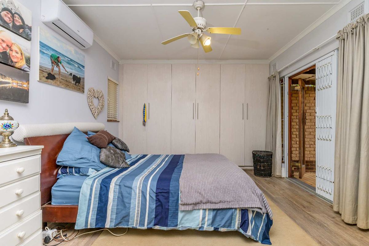 A well-lit bedroom featuring built-in floor-to-ceiling wardrobes, a ceiling fan, and a wall-mounted air conditioning unit, with direct access to an outdoor area.
