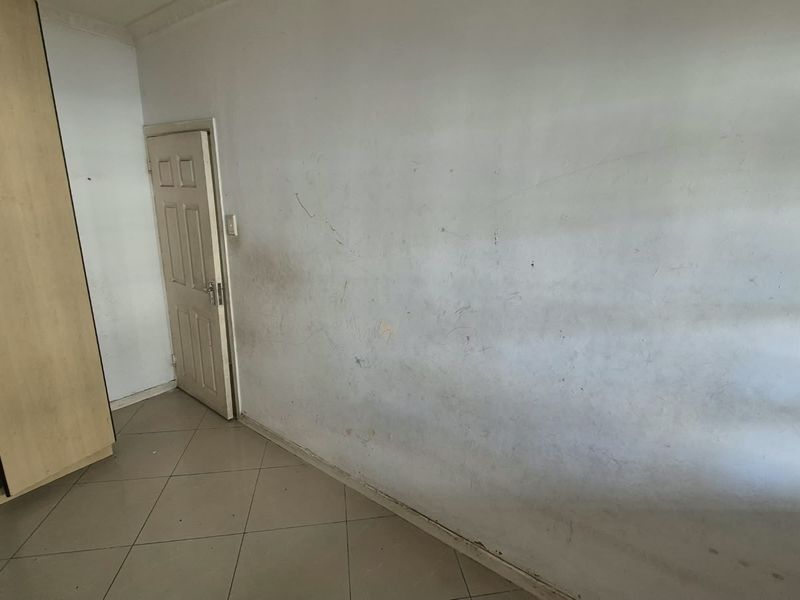 An empty bedroom featuring tiled flooring and a built-in wardrobe, requiring cosmetic updates to the wall finishes.