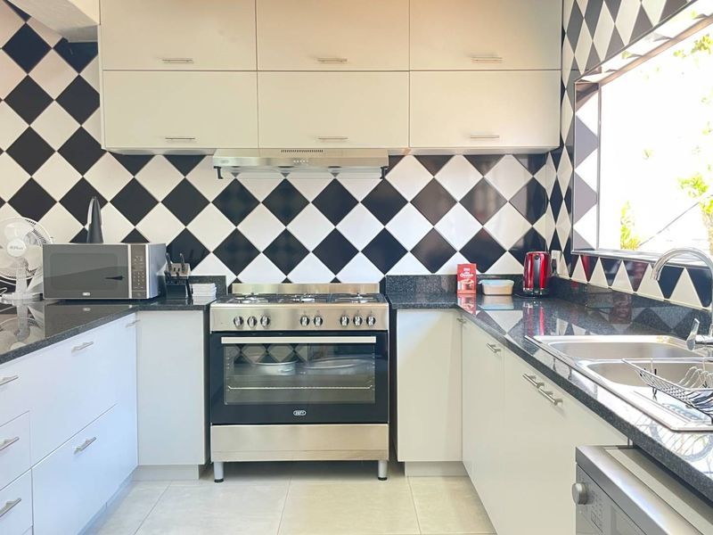 A well-maintained kitchen featuring granite countertops, a stainless steel gas stove with extractor fan, and a distinctive black and white diamond-patterned tiled backsplash.